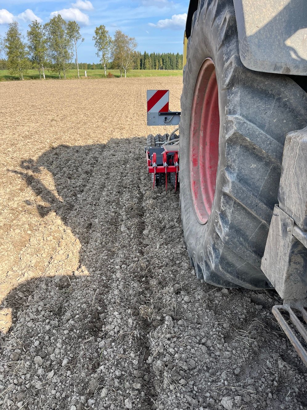 Traktori kyntää peltoa, lähikuva renkaasta ja auran terästä, kun se luo vakoja ruskeaan maahan.