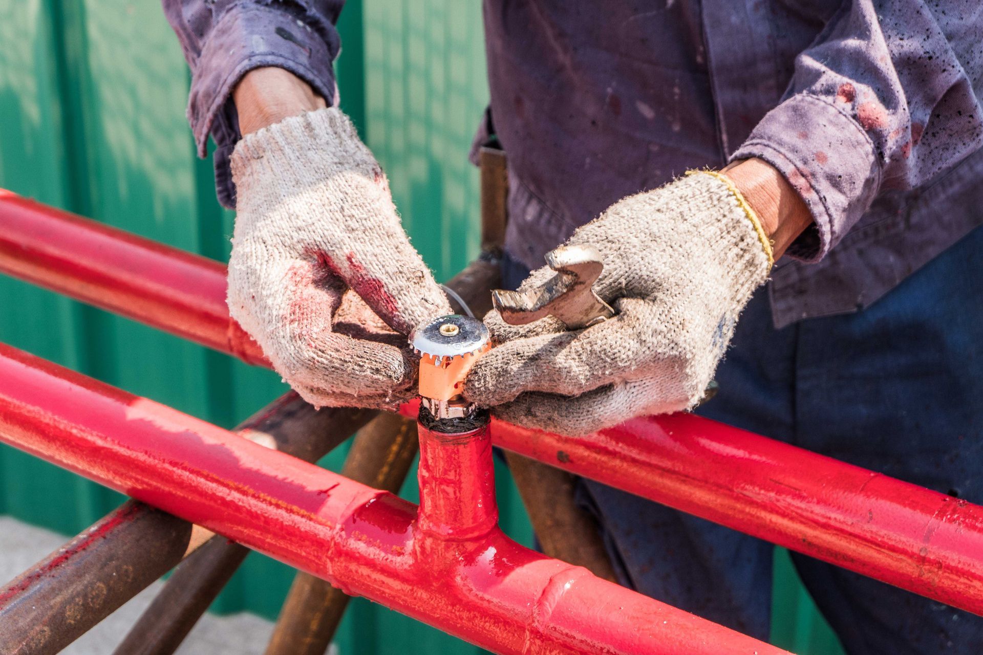Gloved worker tightening a bolt on a red metal railing with a wrench
