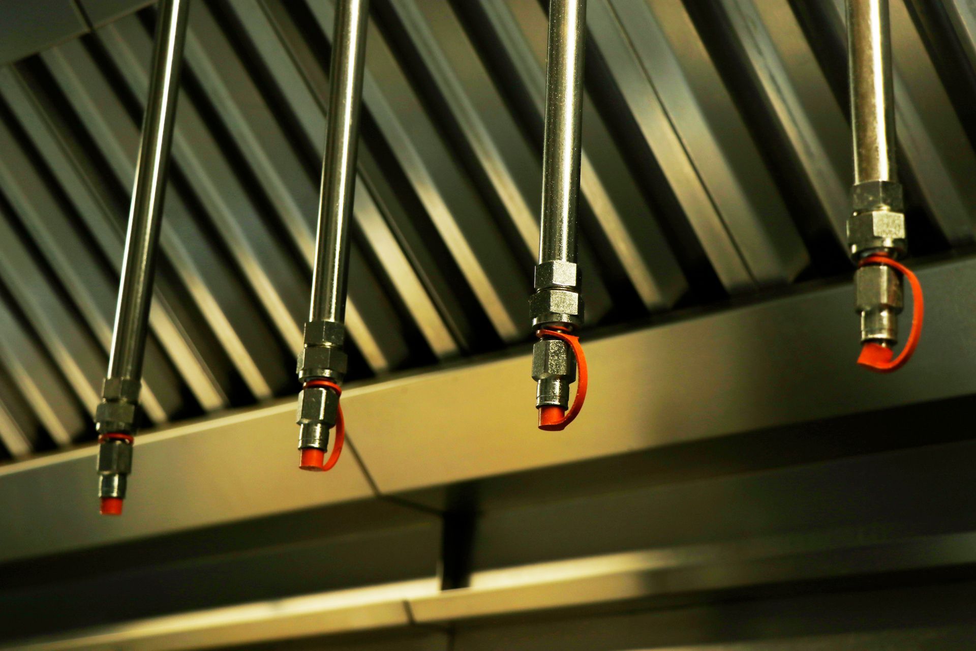 Four hanging metal hoses with red fittings beneath a corrugated industrial ceiling