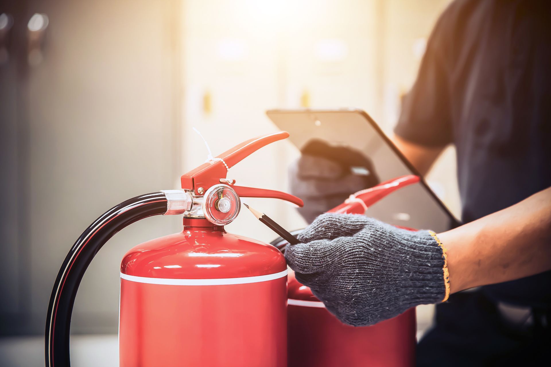 Gloved worker handling a red fire extinguisher with a tablet in the background