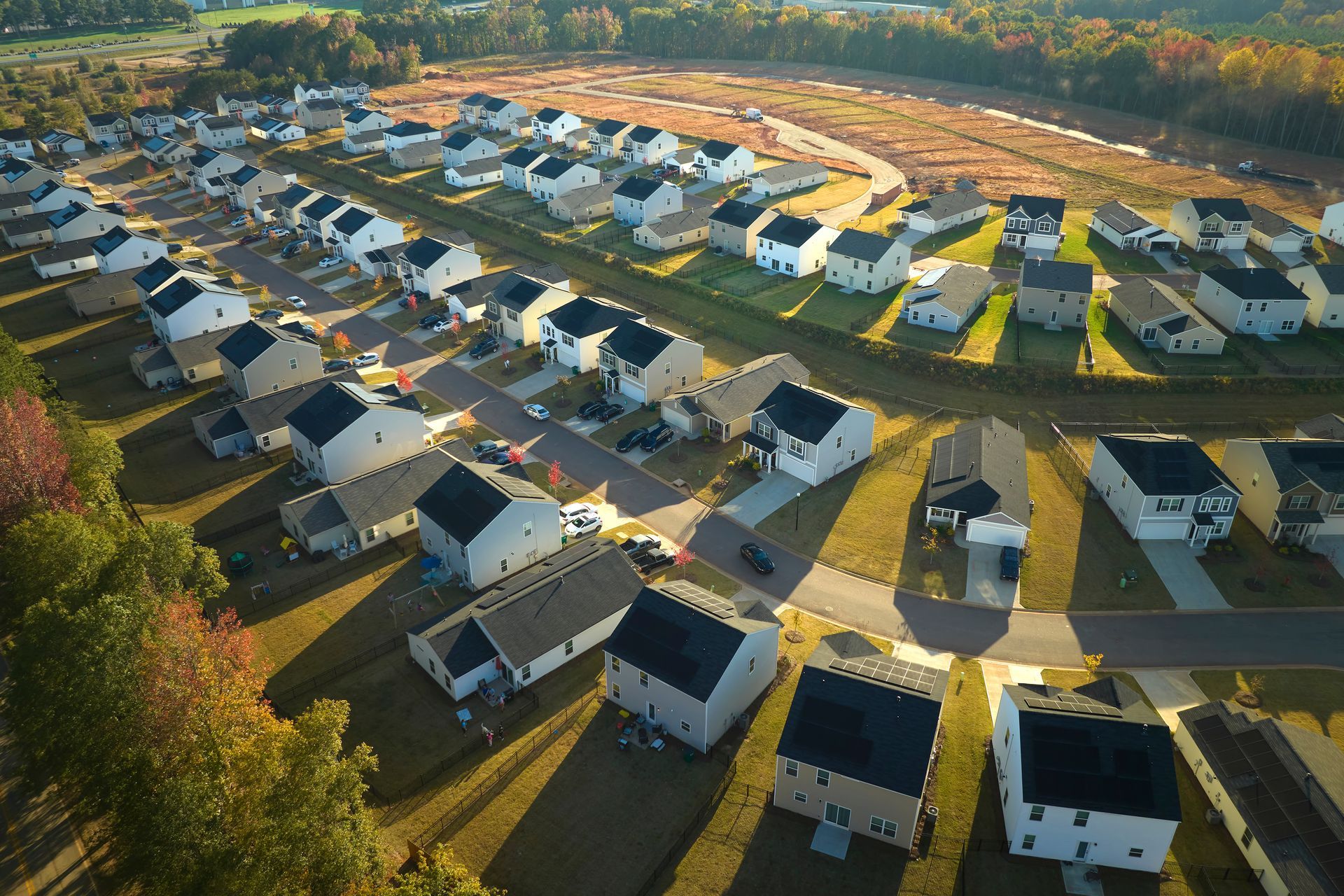 Aerial view of a suburban neighborhood with rows of houses, roads, and green lawns under a cloudy sky.