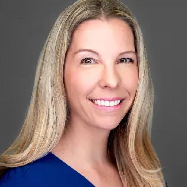 Woman with blonde hair smiling, wearing a blue shirt, against a gray backdrop.