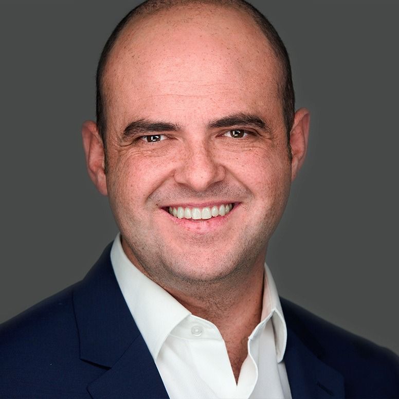 Man in a blue suit smiles broadly, against a gray backdrop.