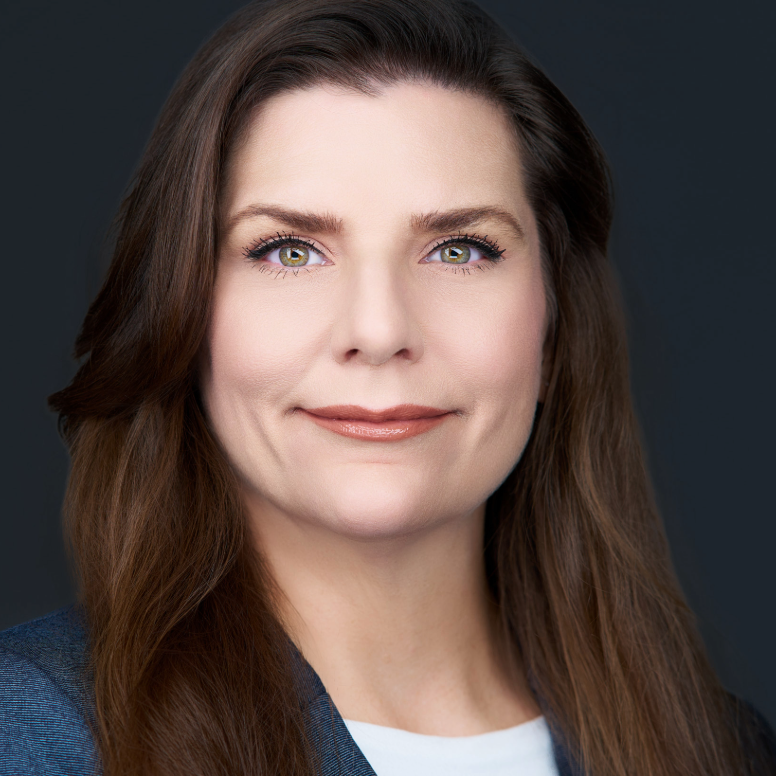 Woman with long brown hair, wearing a white shirt and blue blazer, smiling at the camera.