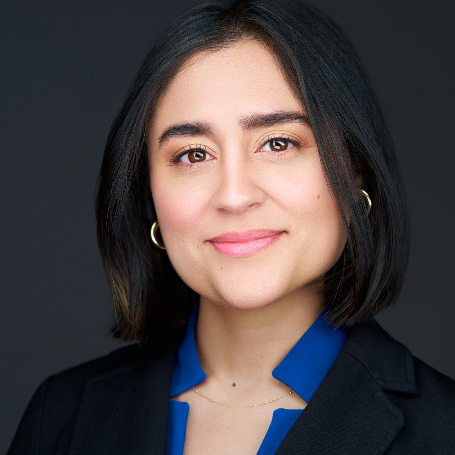 Woman with short black hair, wearing a blazer over a blue top, smiling at the camera.