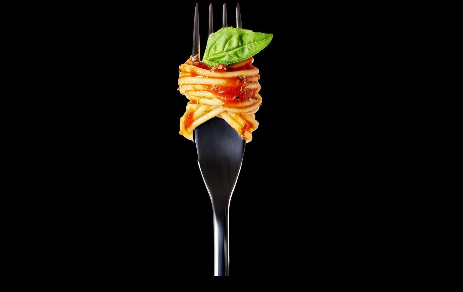 A fork with spaghetti and basil on it on a black background.