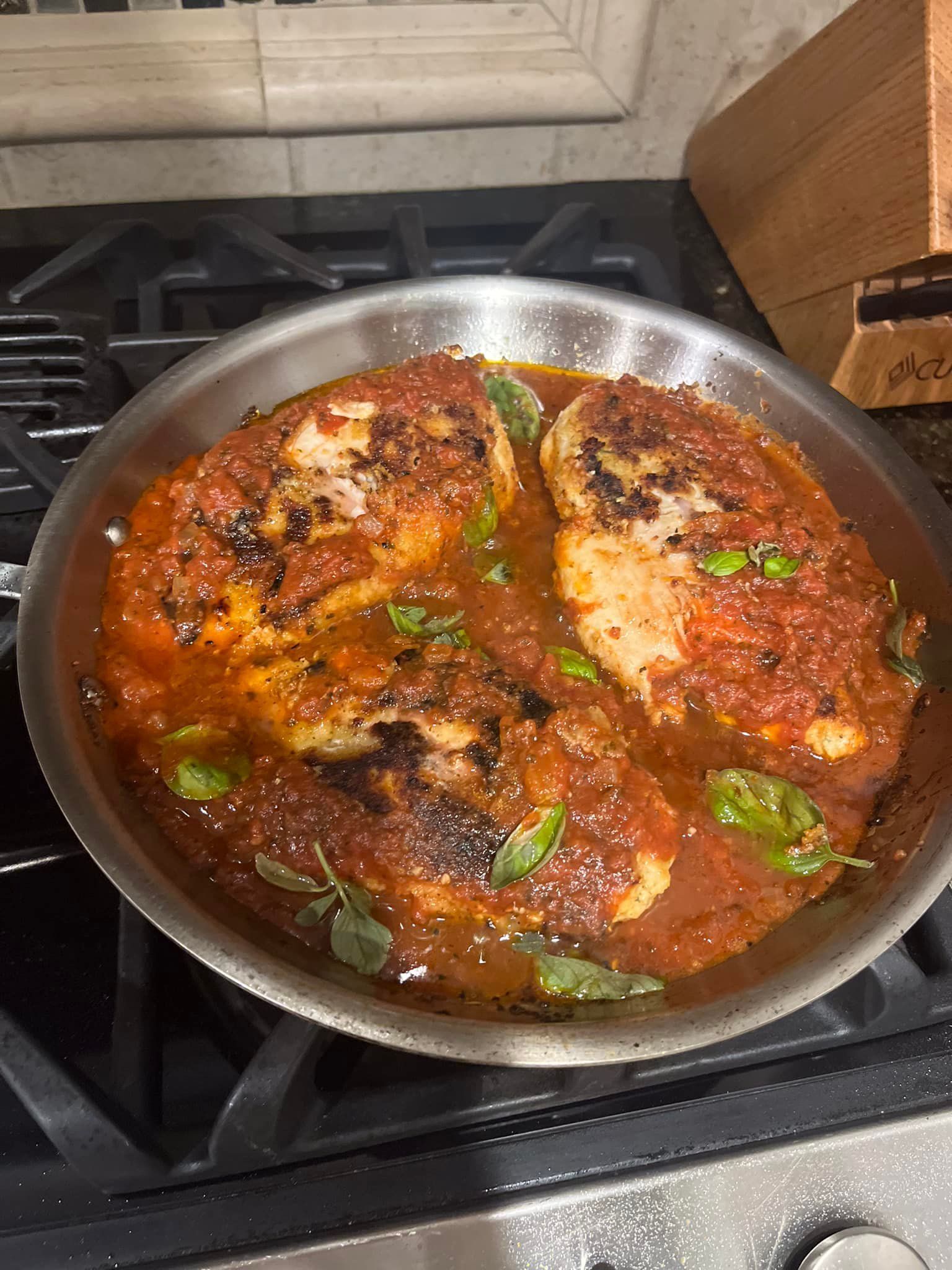 A pan filled with chicken and tomato sauce on a stove.