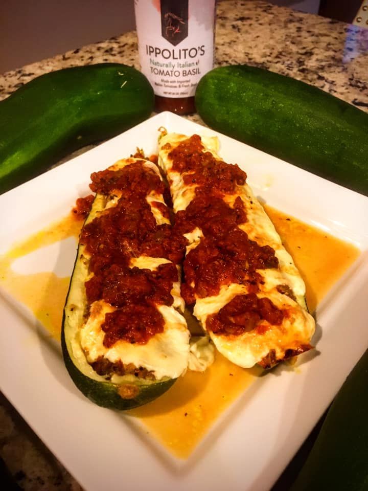 A white plate topped with stuffed zucchini next to a bottle of ippolito 's hot sauce