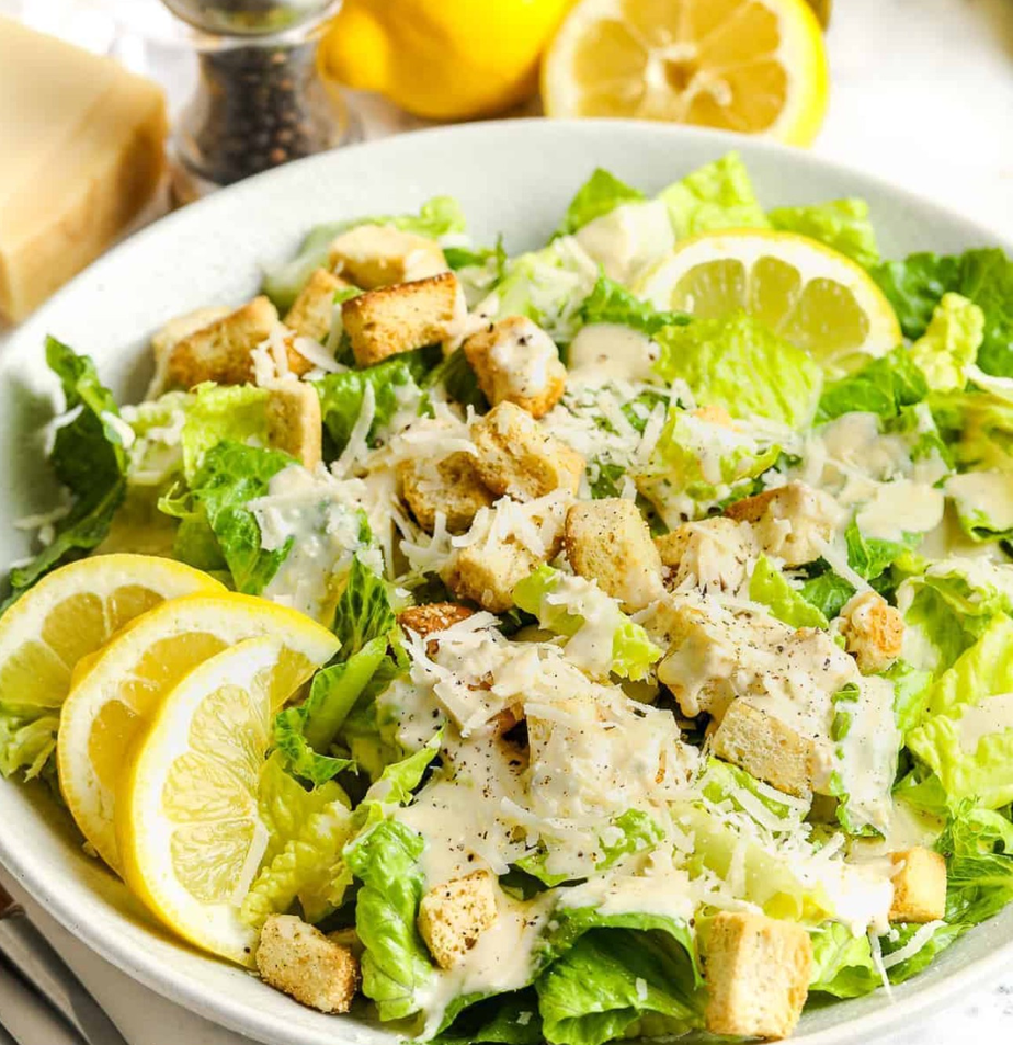 A salad with lettuce , croutons , cheese and lemon slices on a plate.