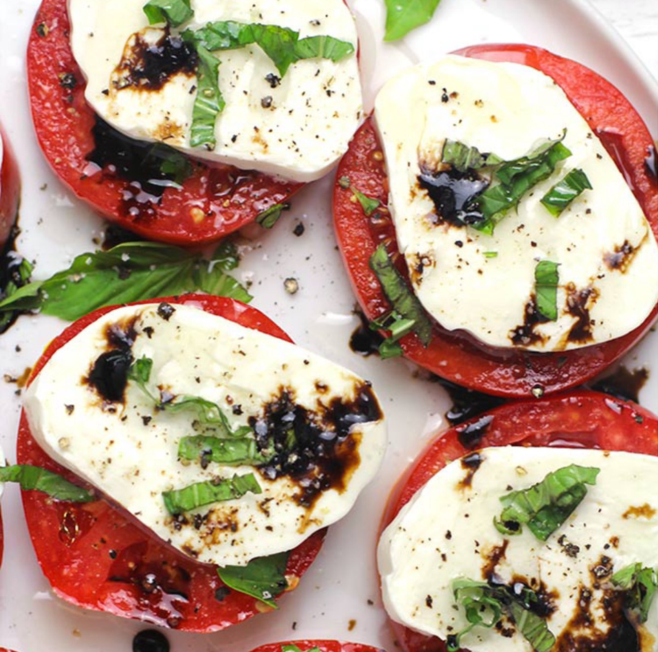 A white plate topped with sliced tomatoes and mozzarella cheese