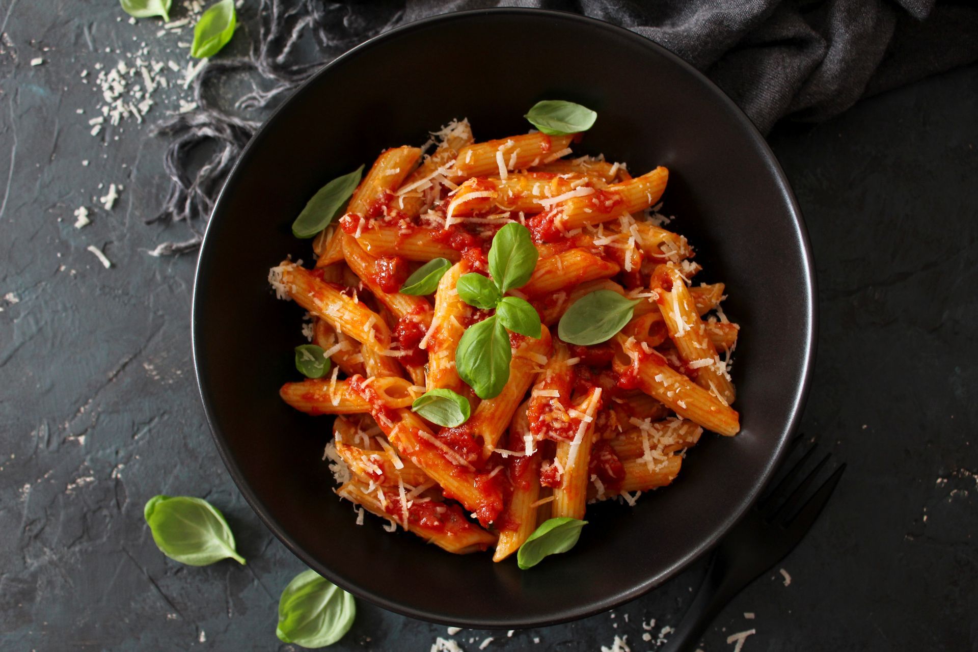 A bowl of pasta with tomato sauce and basil on a table.