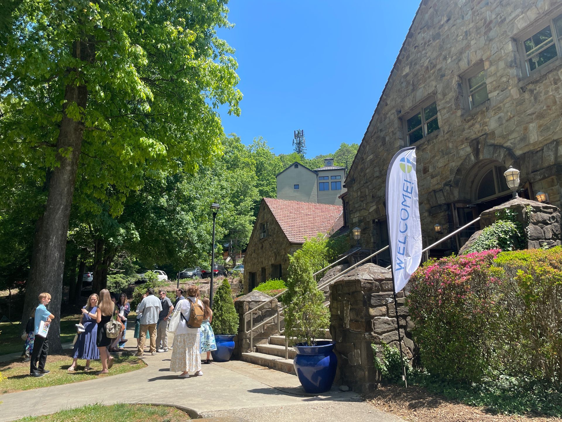 People walking through a sunny stone courtyard beside a stone chapel.