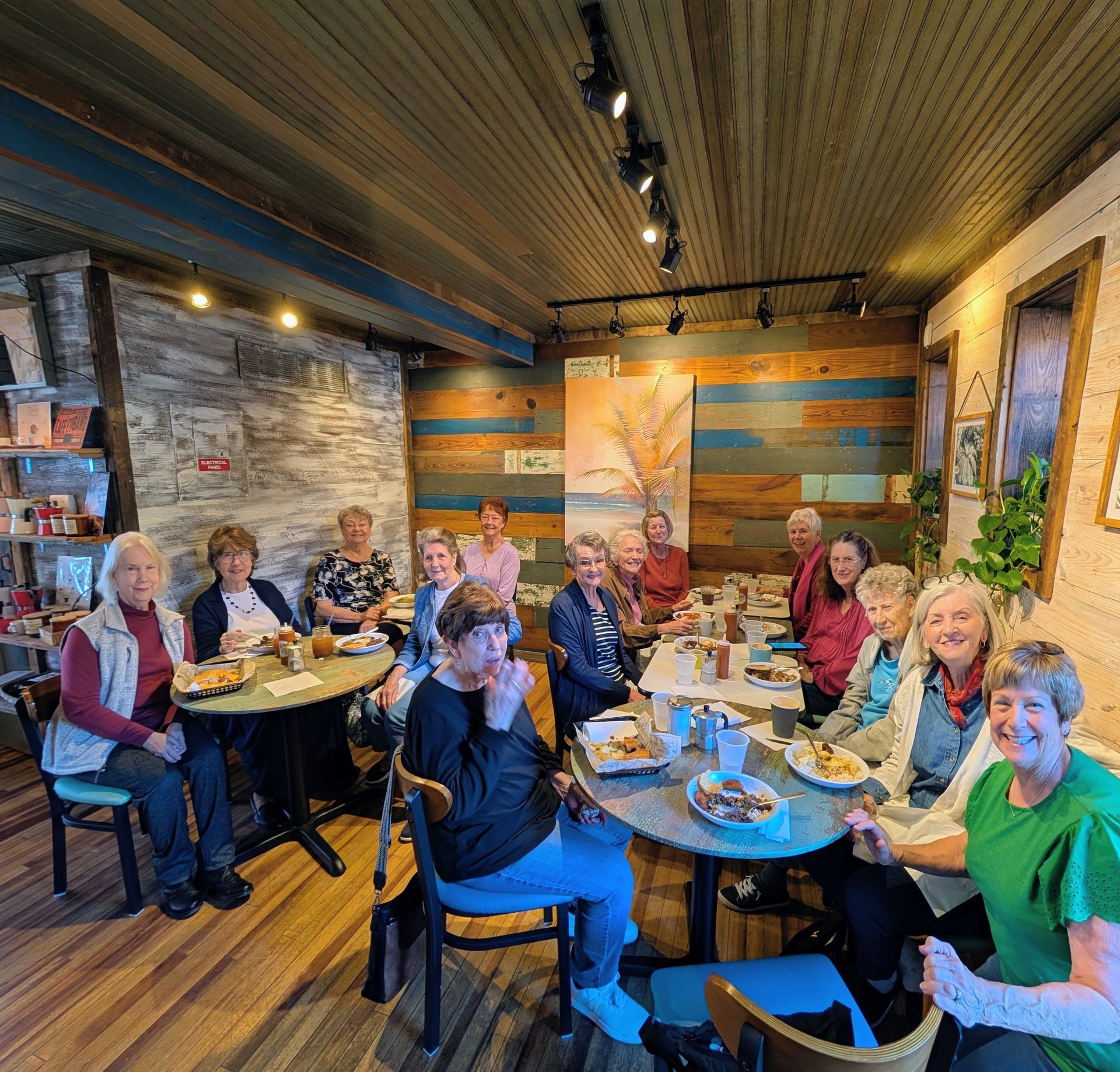 Group of people sitting at tables in a cozy restaurant, smiling and chatting under warm lighting.