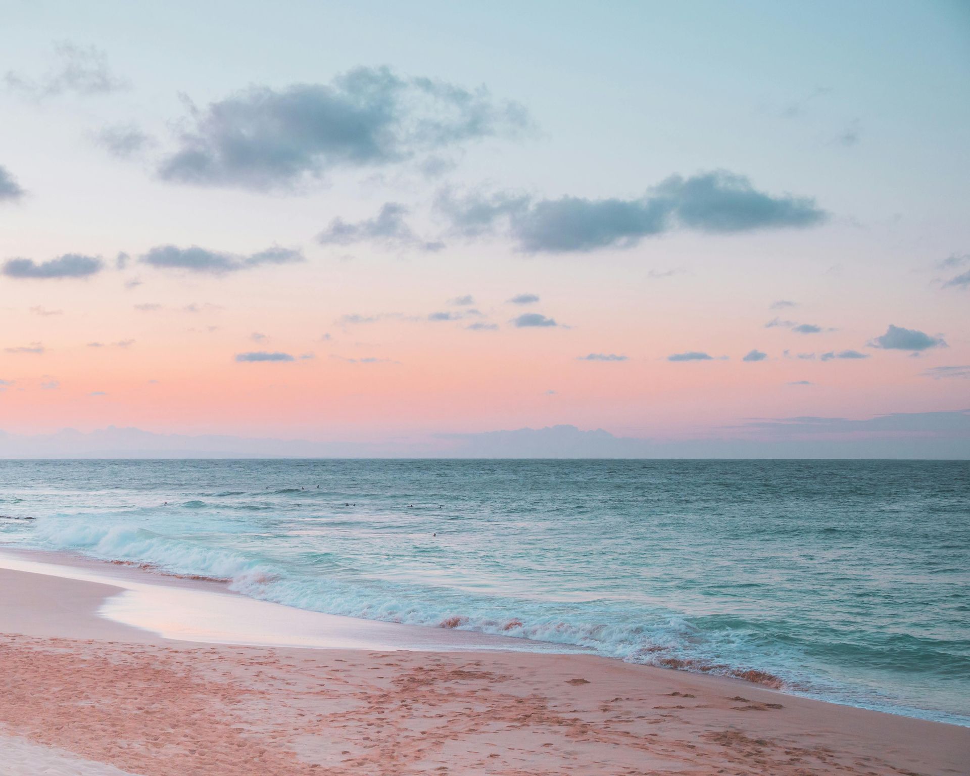 Pink and blue beach sunset with gentle waves and clouds.