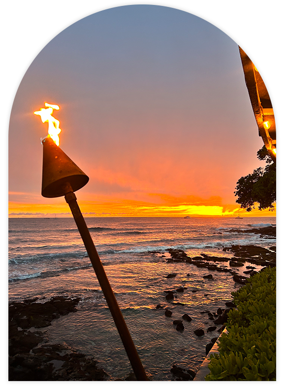 A tiki torch burning brightly against a vibrant sunset over the ocean.