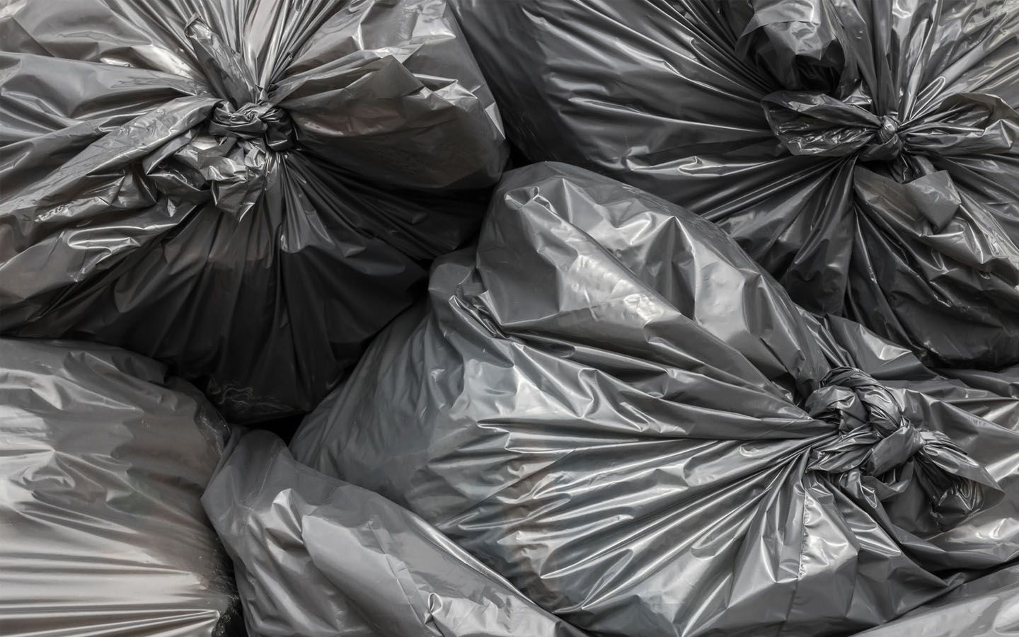 A pile of gray garbage bags are stacked on top of each other.