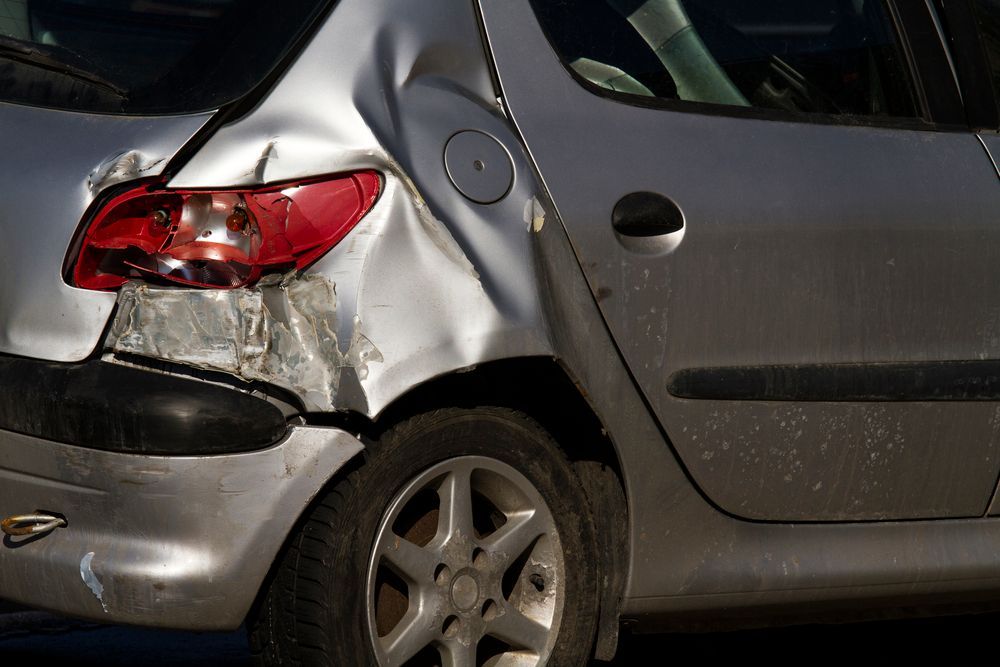 A silver car with a damaged bumper is at a scrap yard