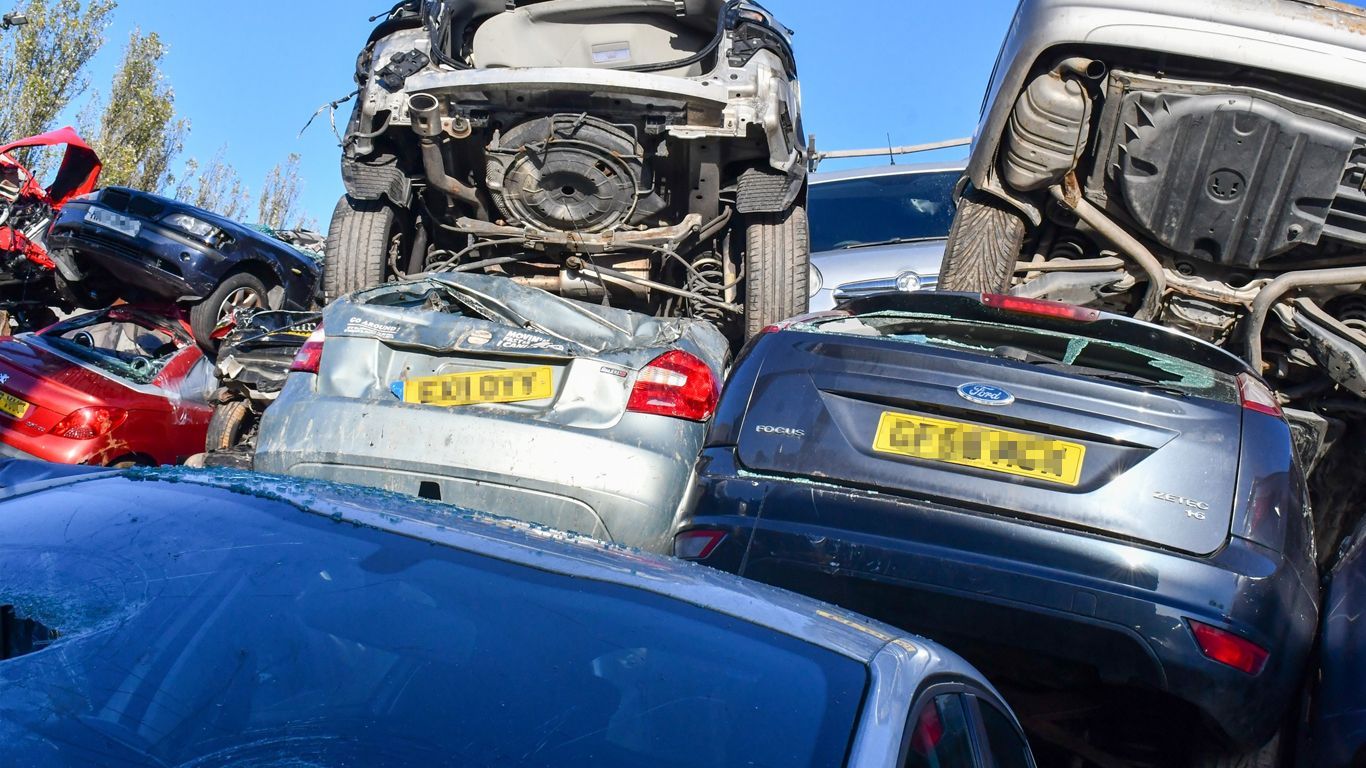 A bunch of cars are stacked on top of each other in a scrap yard waiting to be scrapped