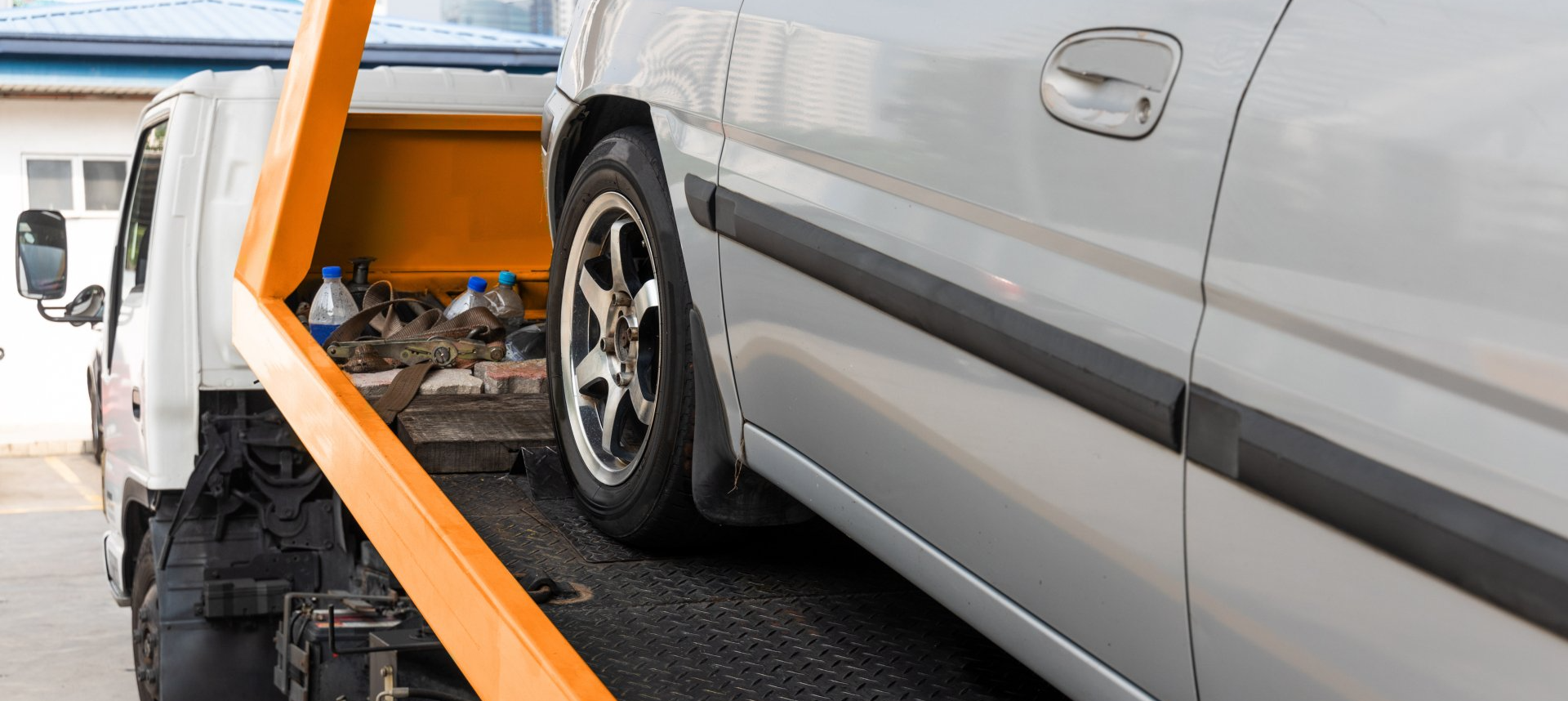 A silver car is being towed by a tow truck to Benfleet Scrap to be scrapped