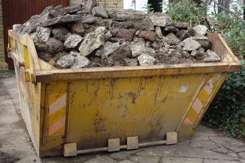 A large yellow skip filled with rocks and dirt.