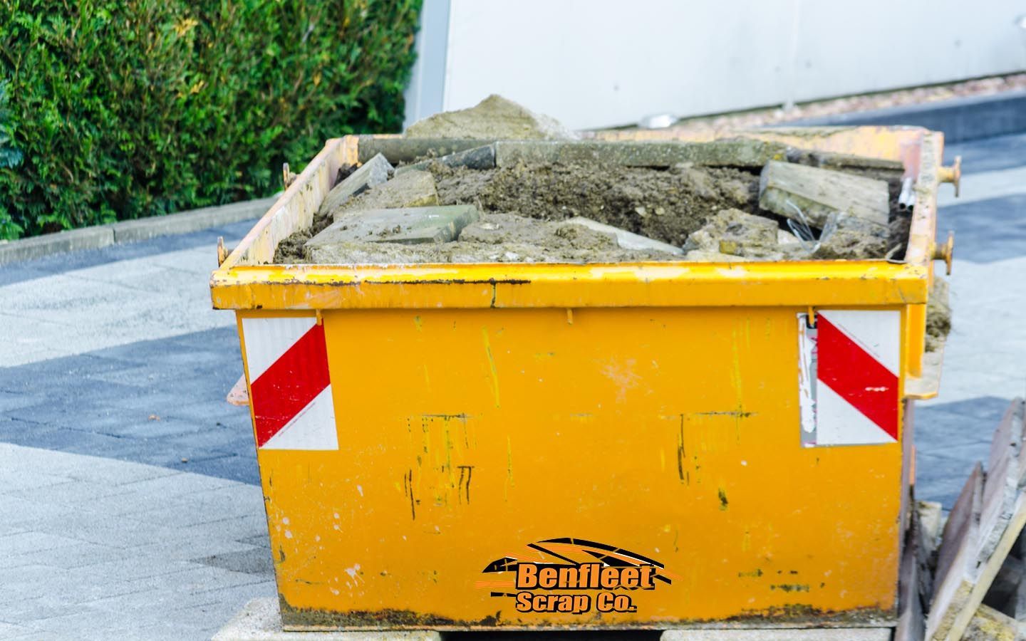 A yellow skip is filled with dirt and rocks with Benfleet Scrap logo