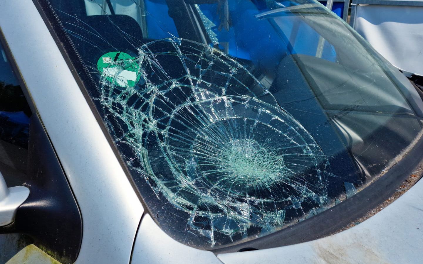 A car with a broken windscreen is parked on the side of the road.