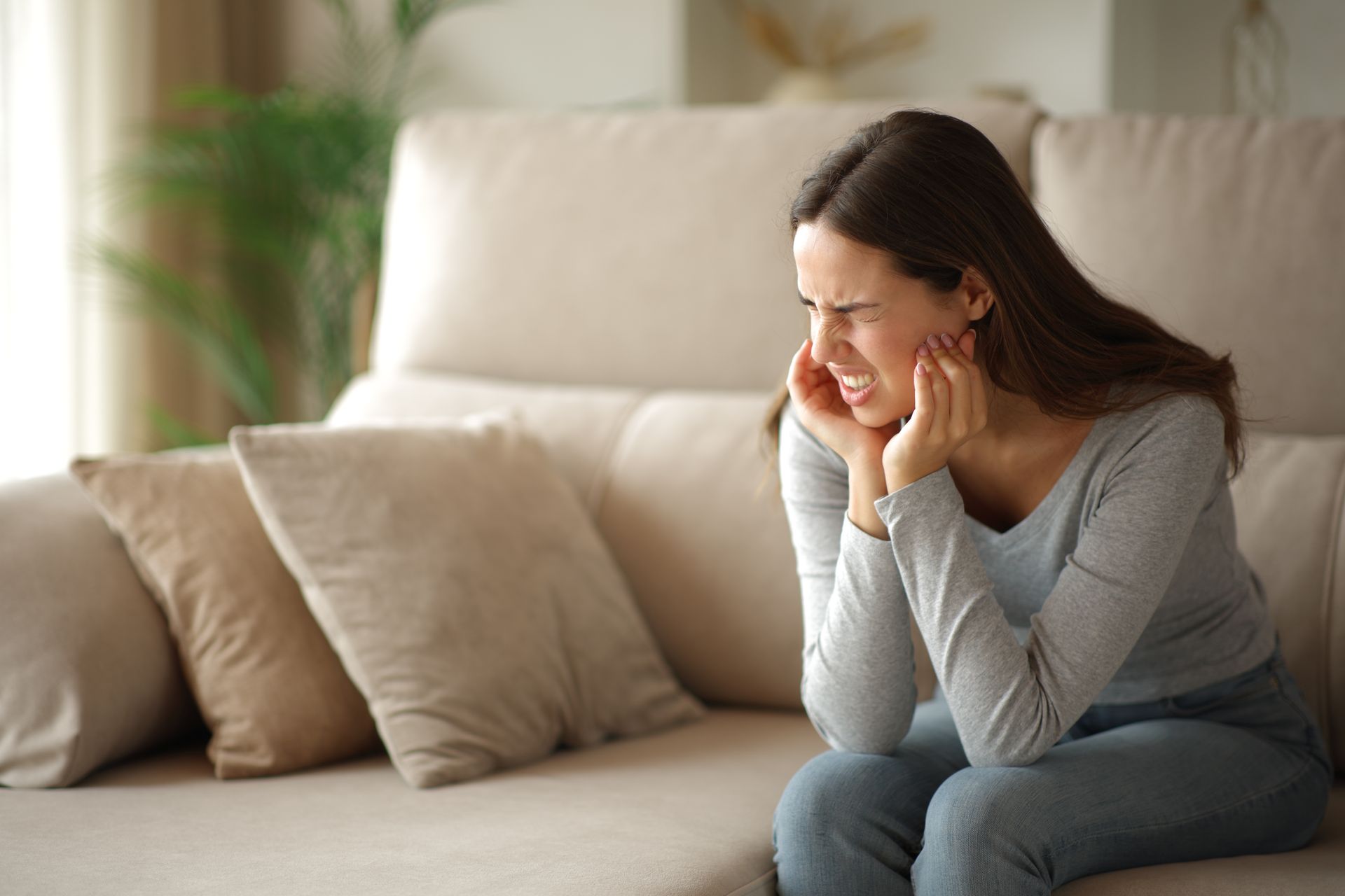 Woman on a couch holding her face, appearing to be in pain, indoors.