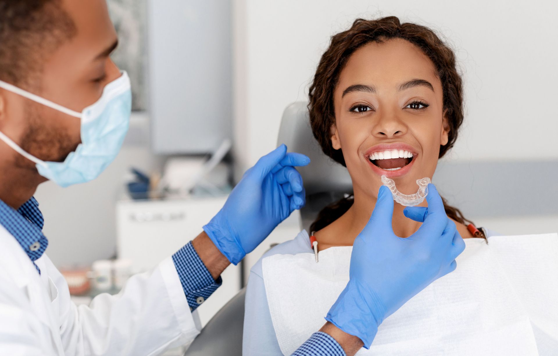 Dentist holding clear aligner near patient's mouth in dental office.