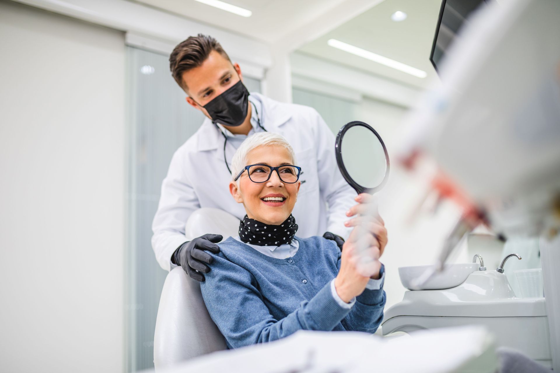 Dentist showing a patient their teeth in a mirror. Both are smiling in a dental office.