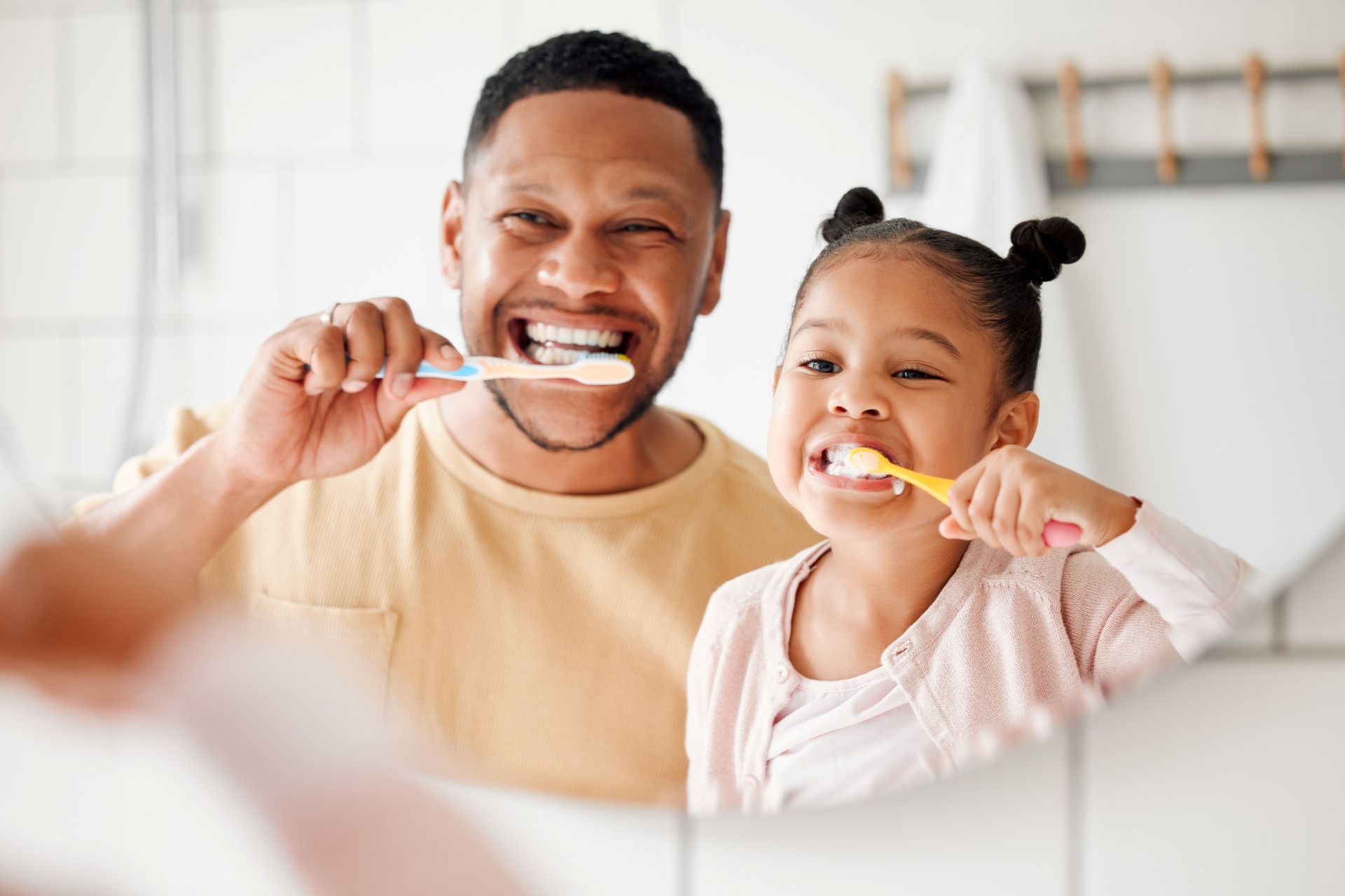 Father and child brushing teeth together in a bathroom, smiling with toothbrushes.