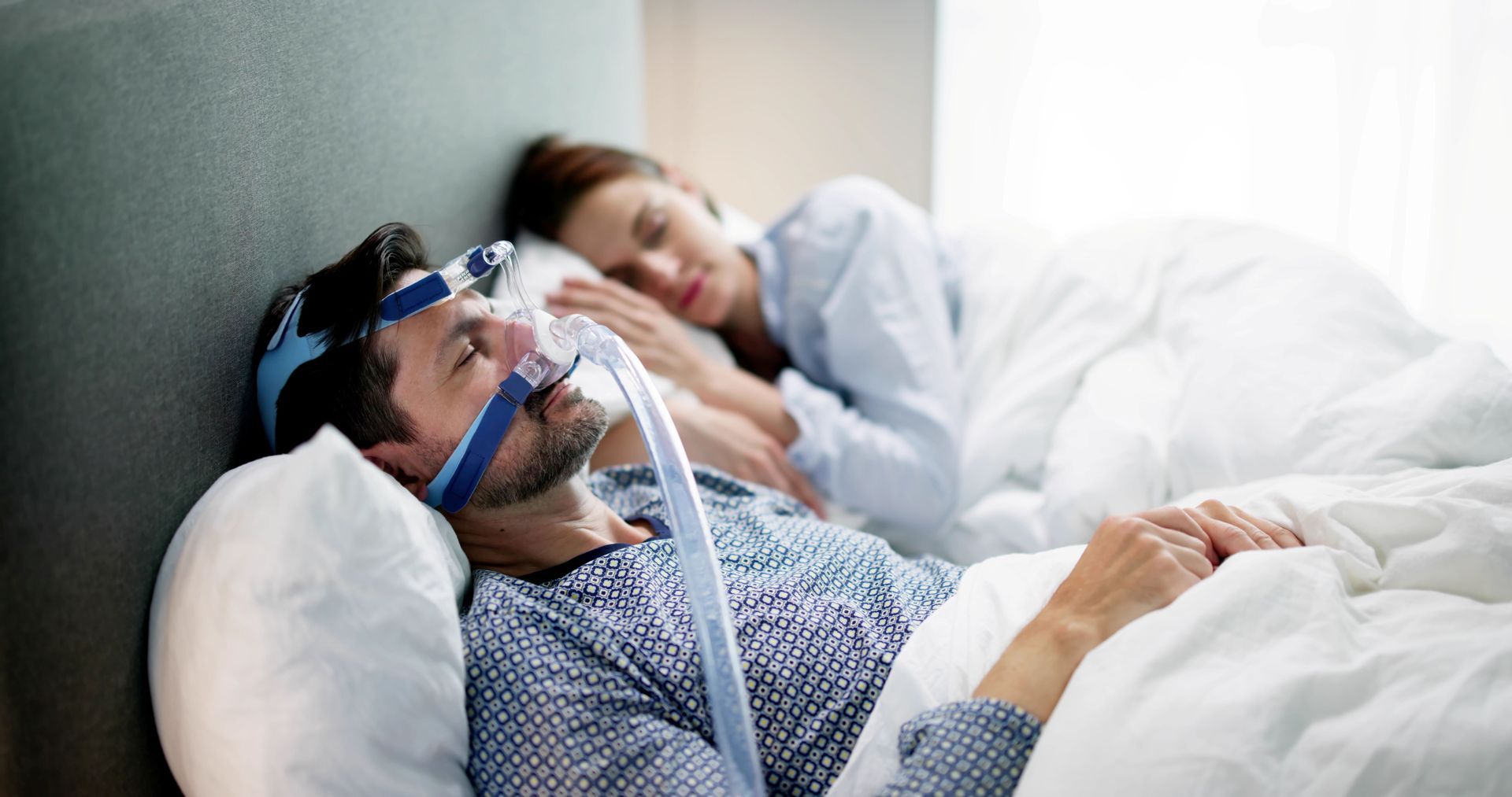 Man wearing CPAP mask sleeping in bed with a person beside him.