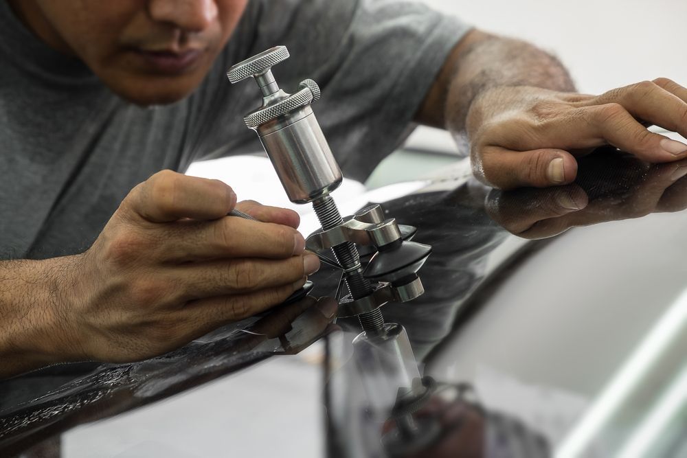 Technician using a handheld tool to repair a car windshield chip