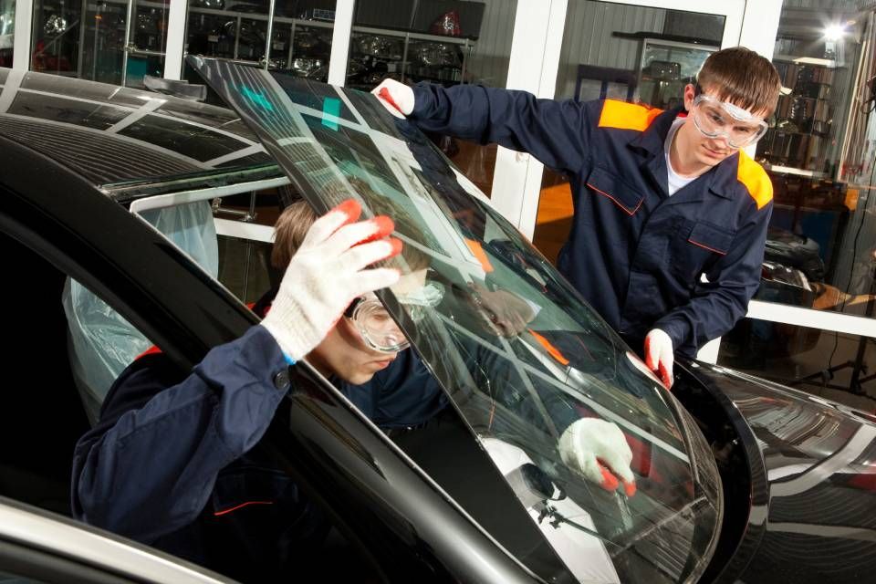 Mechanic inspecting a car windshield while another technician assists in a garage