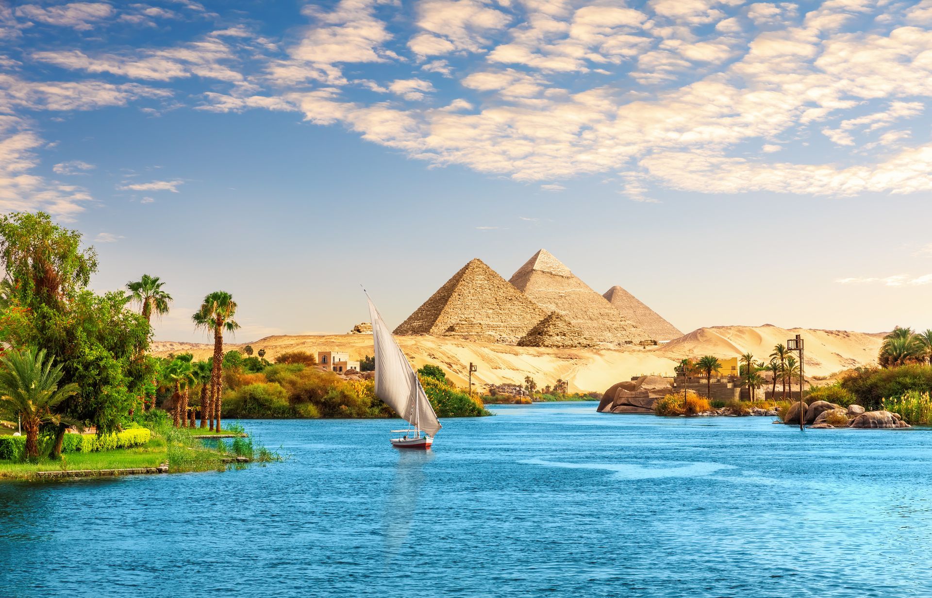 A sailboat is floating on a river with pyramids in the background.