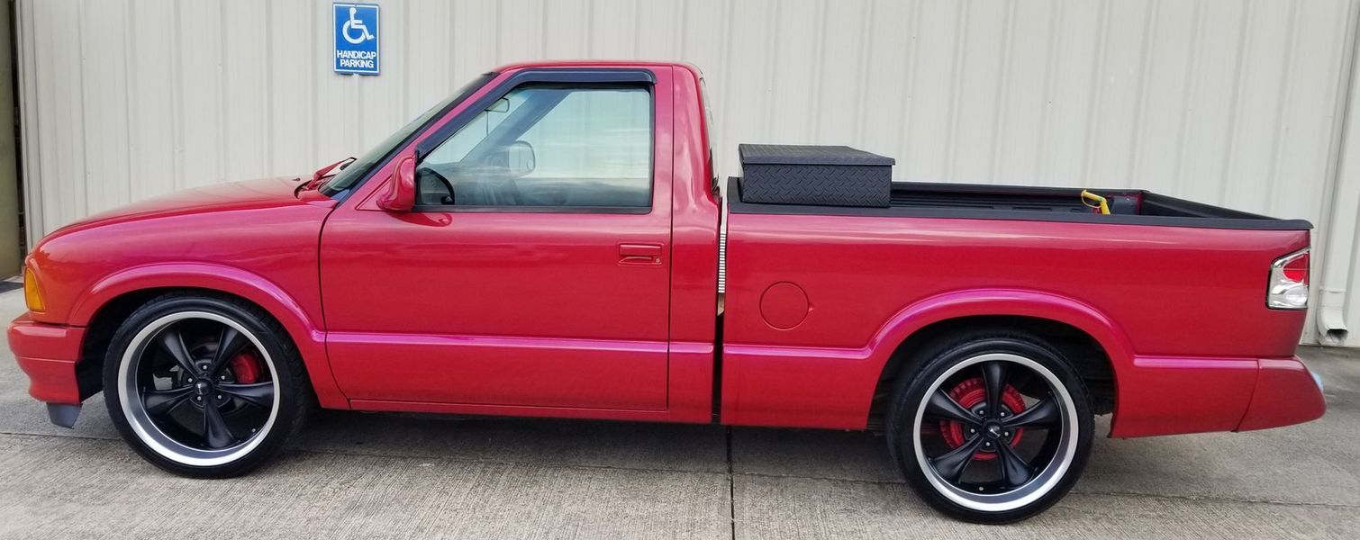 A red pickup truck is parked in front of a handicapped parking spot.