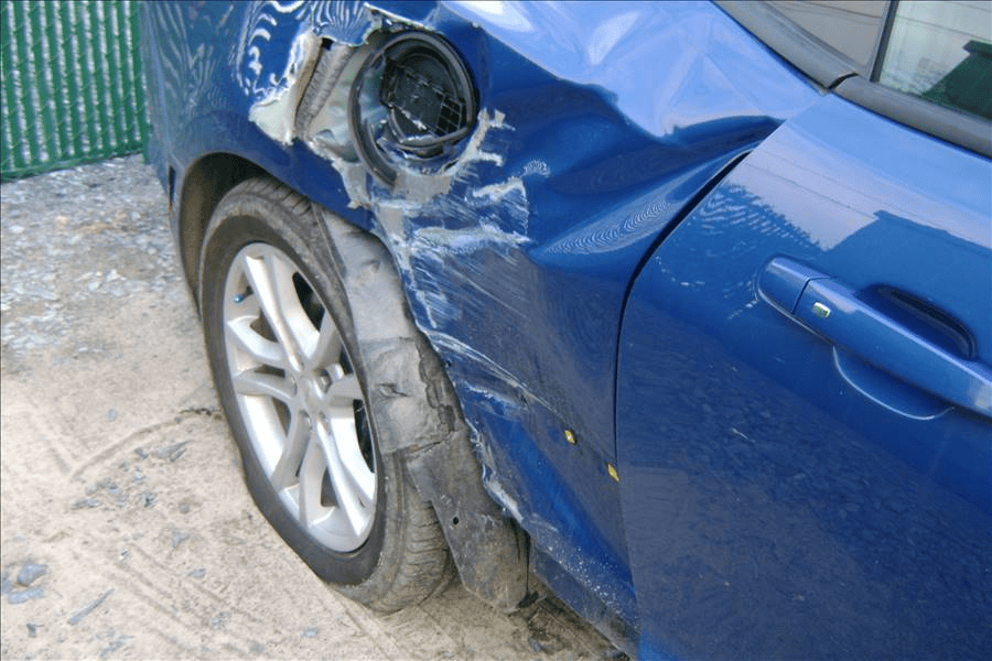 A blue car with a damaged fender is parked on the side of the road