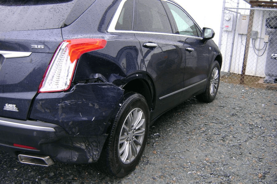 A blue car with a damaged side is parked in a gravel lot.