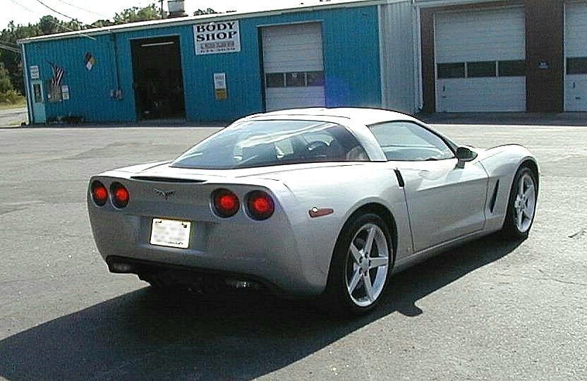 A silver sports car is parked in front of a body shop