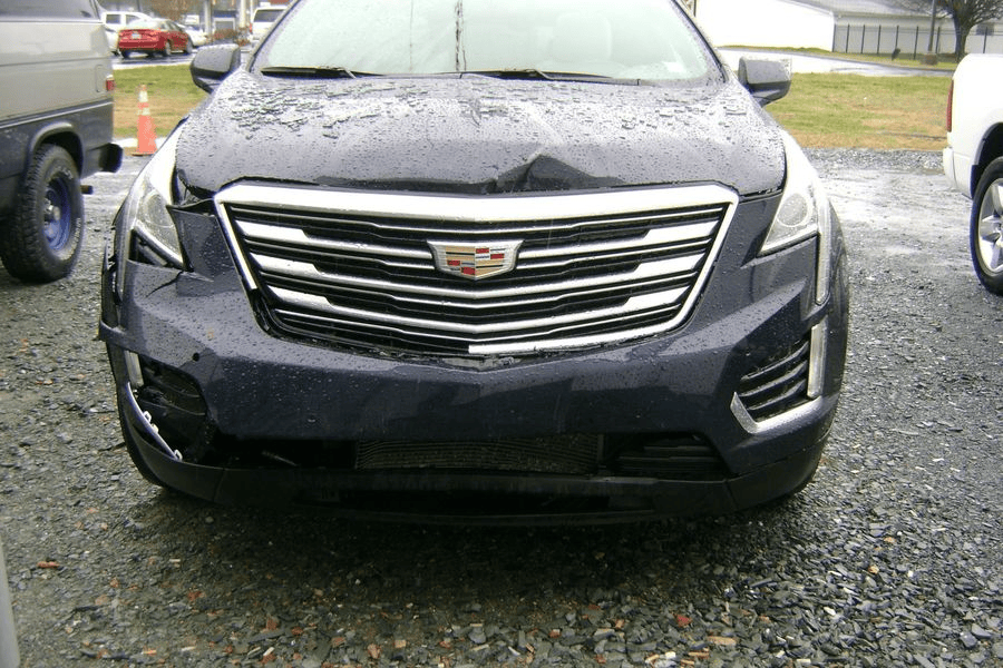 A black cadillac is parked in a gravel lot.