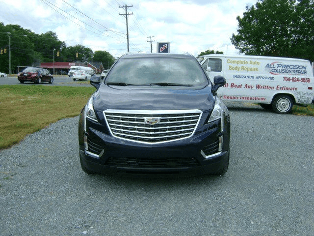 A blue cadillac is parked on the side of the road next to a white van.