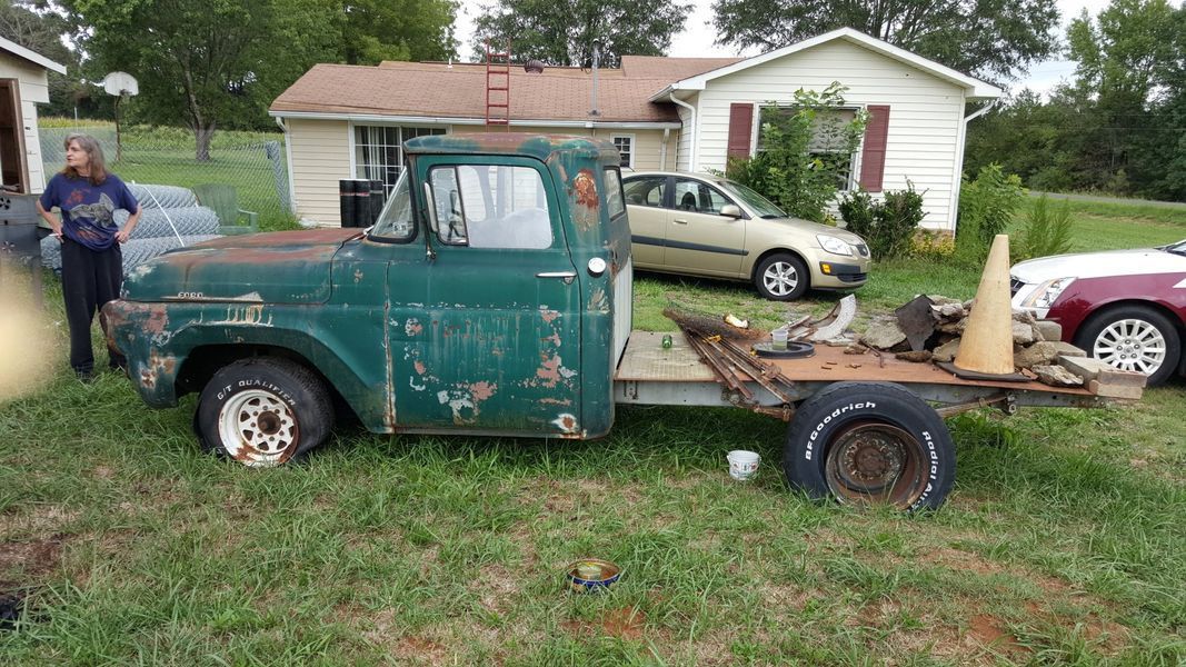 A green truck is parked in a grassy field in front of a house.