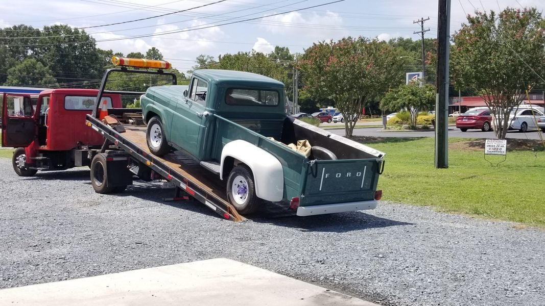 A green truck is being towed by a tow truck.