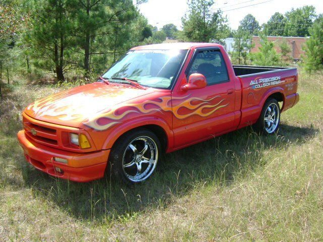 A red truck with flames painted on it is parked in a field