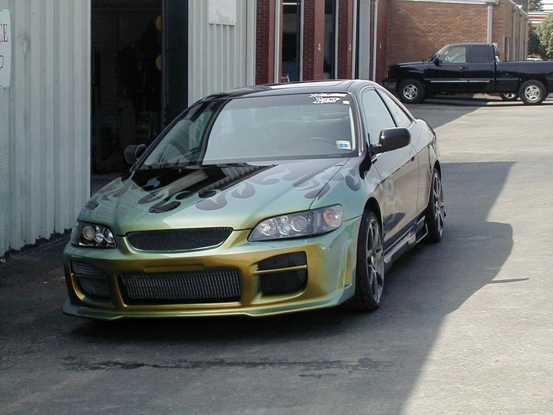 A green and yellow car is parked in front of a building