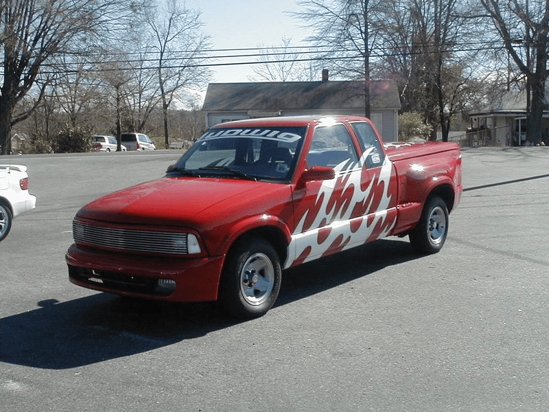 A red truck with a checkered pattern on the side is parked in a parking lot