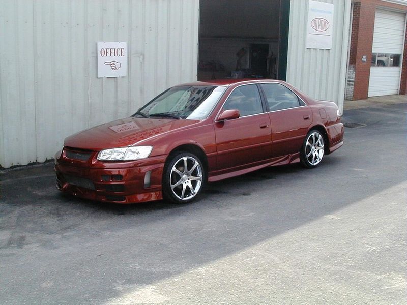 A red car is parked in front of a white building