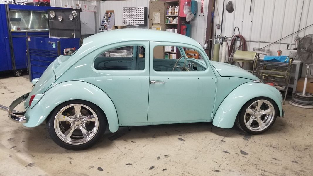 A light blue volkswagen beetle is parked in a garage.