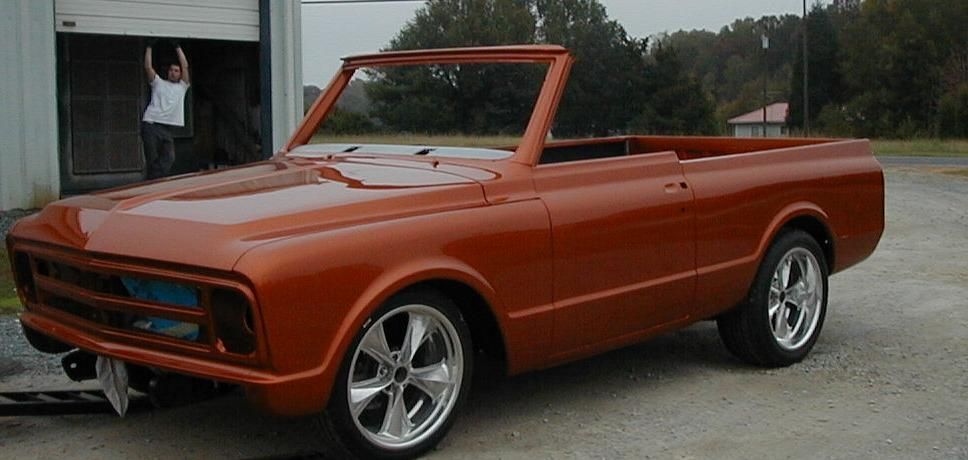 A man in a white shirt is standing next to an orange car
