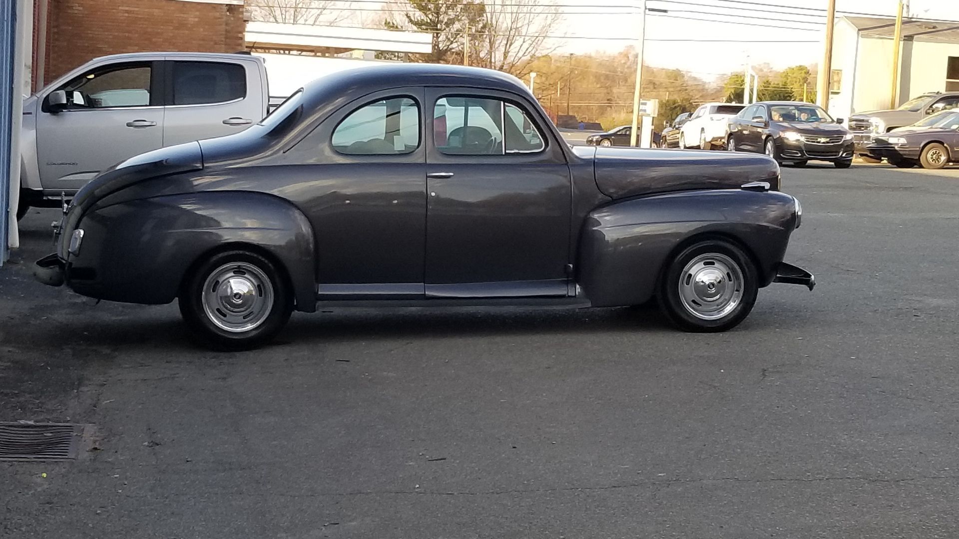 An old car is parked in a parking lot next to a truck.