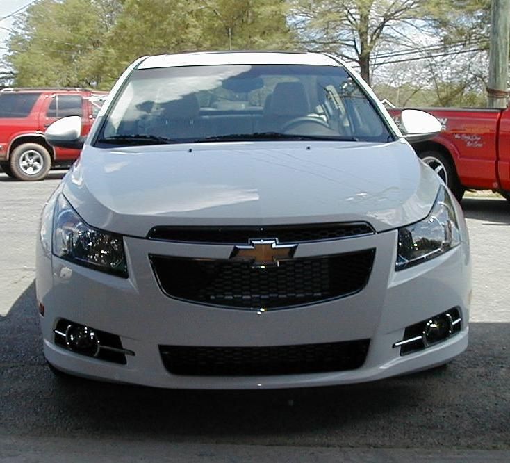 A white chevrolet car is parked next to a red truck